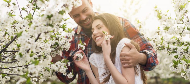Young, heterosexual couple enjoying among trees in bloom.